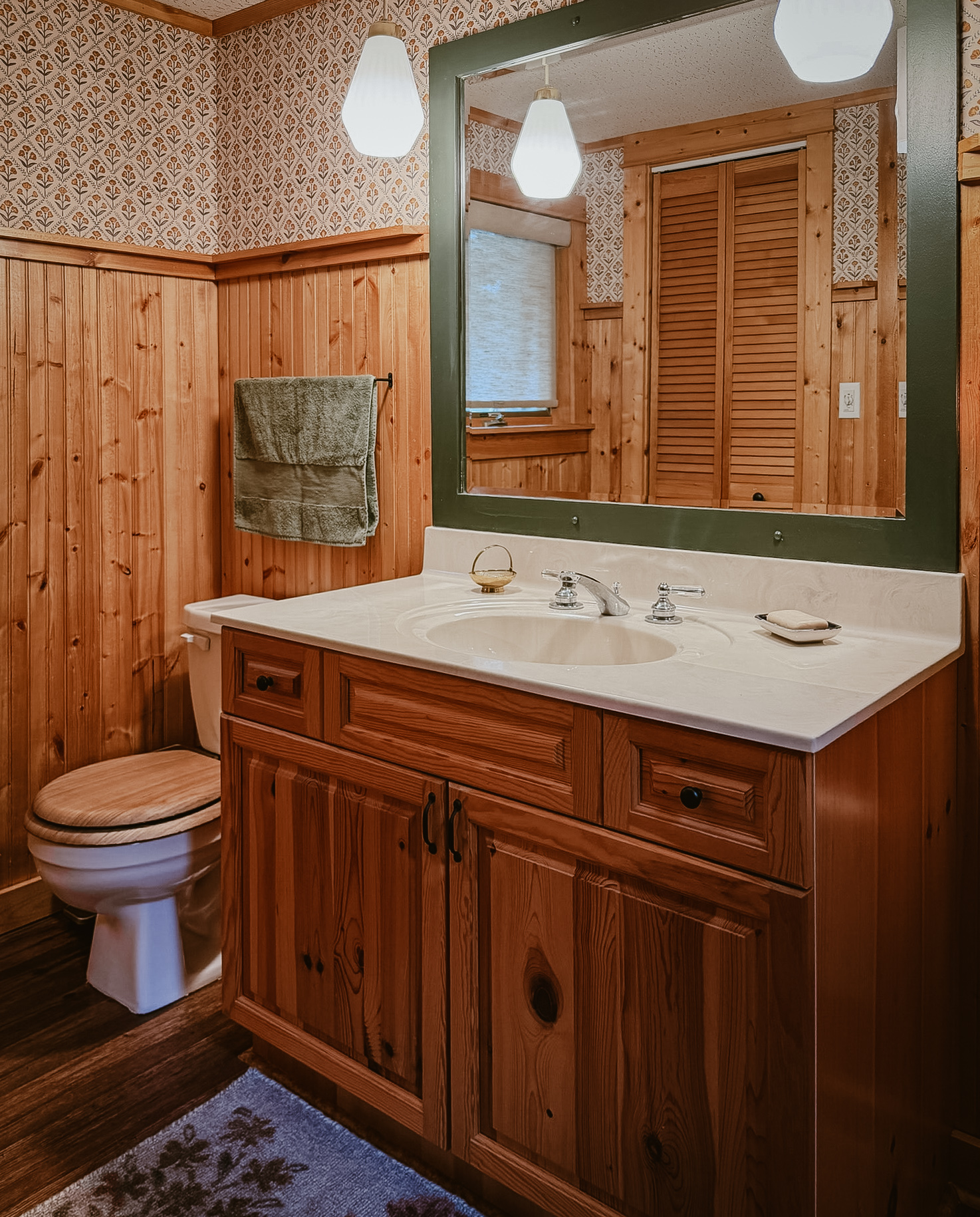 The cabin bathroom with wood-paneled walls and a green-trimmed mirror
