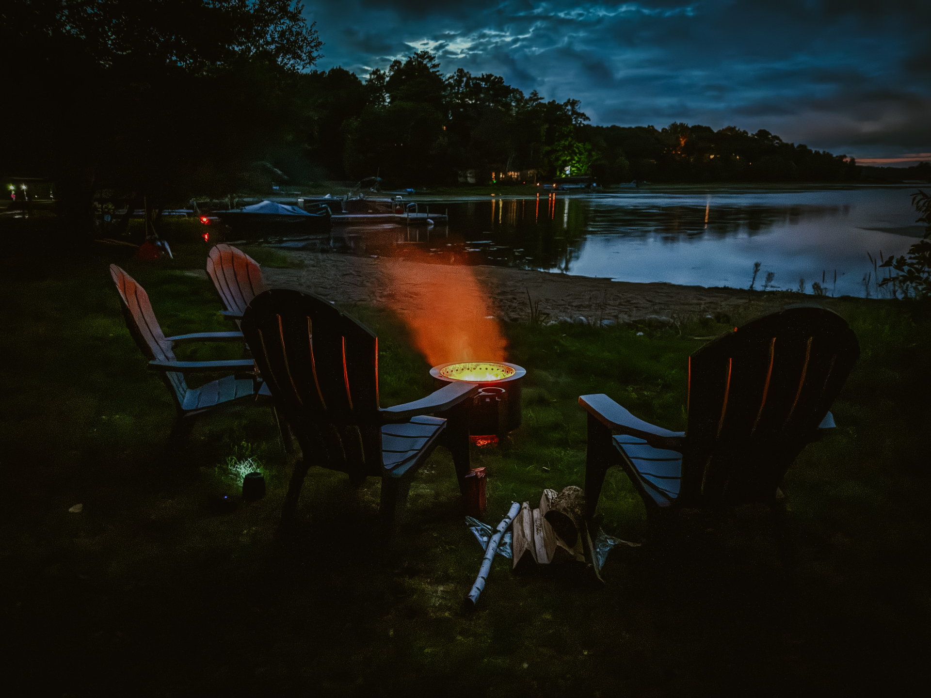 The fire pit glowing at dusk between lawn chairs, with the lake and dock beyond