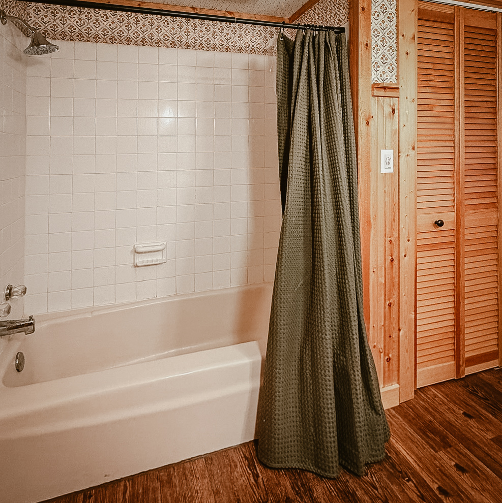 The bathroom shower and tub with white tile and a green curtain