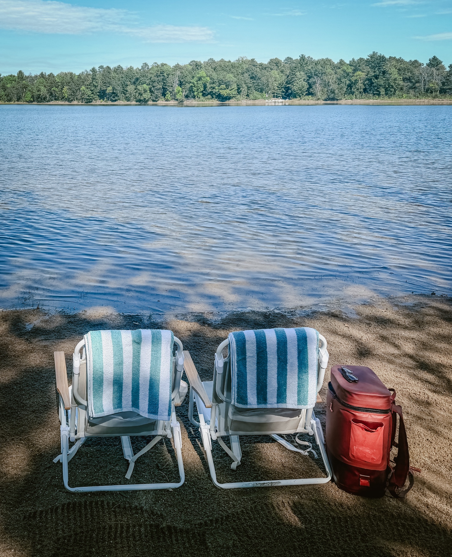 Two beach chairs on the sandy shore looking out over the lake
