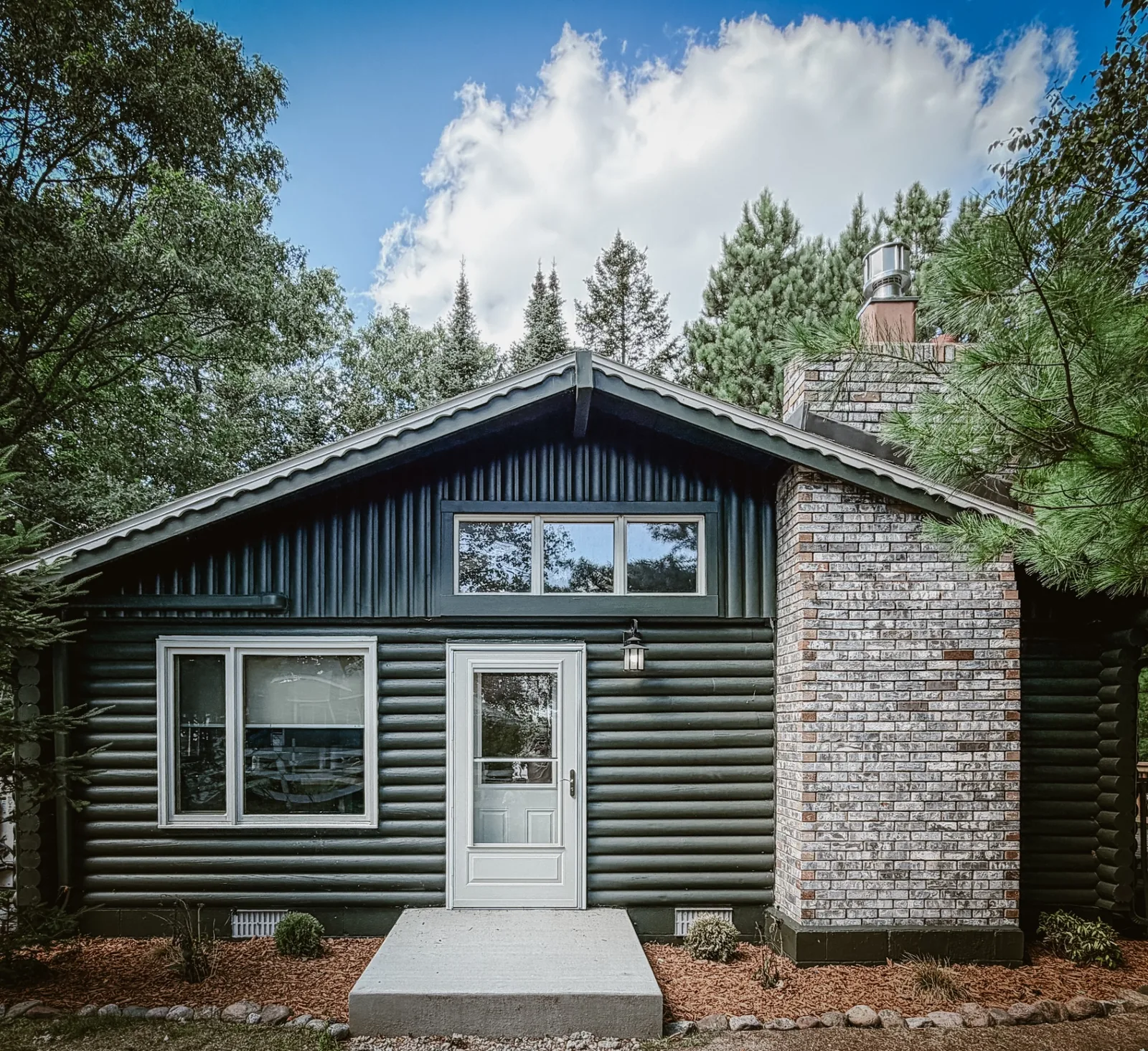 The dark green log cabin tucked among tall pines