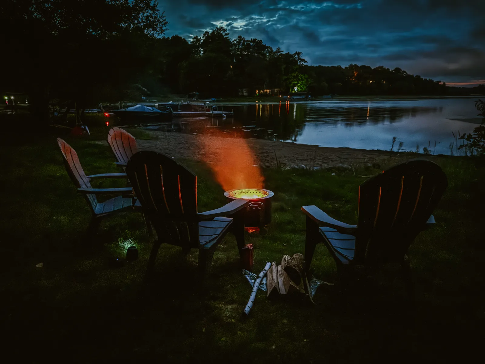 The fire pit glowing at dusk between lawn chairs, with the lake and dock beyond