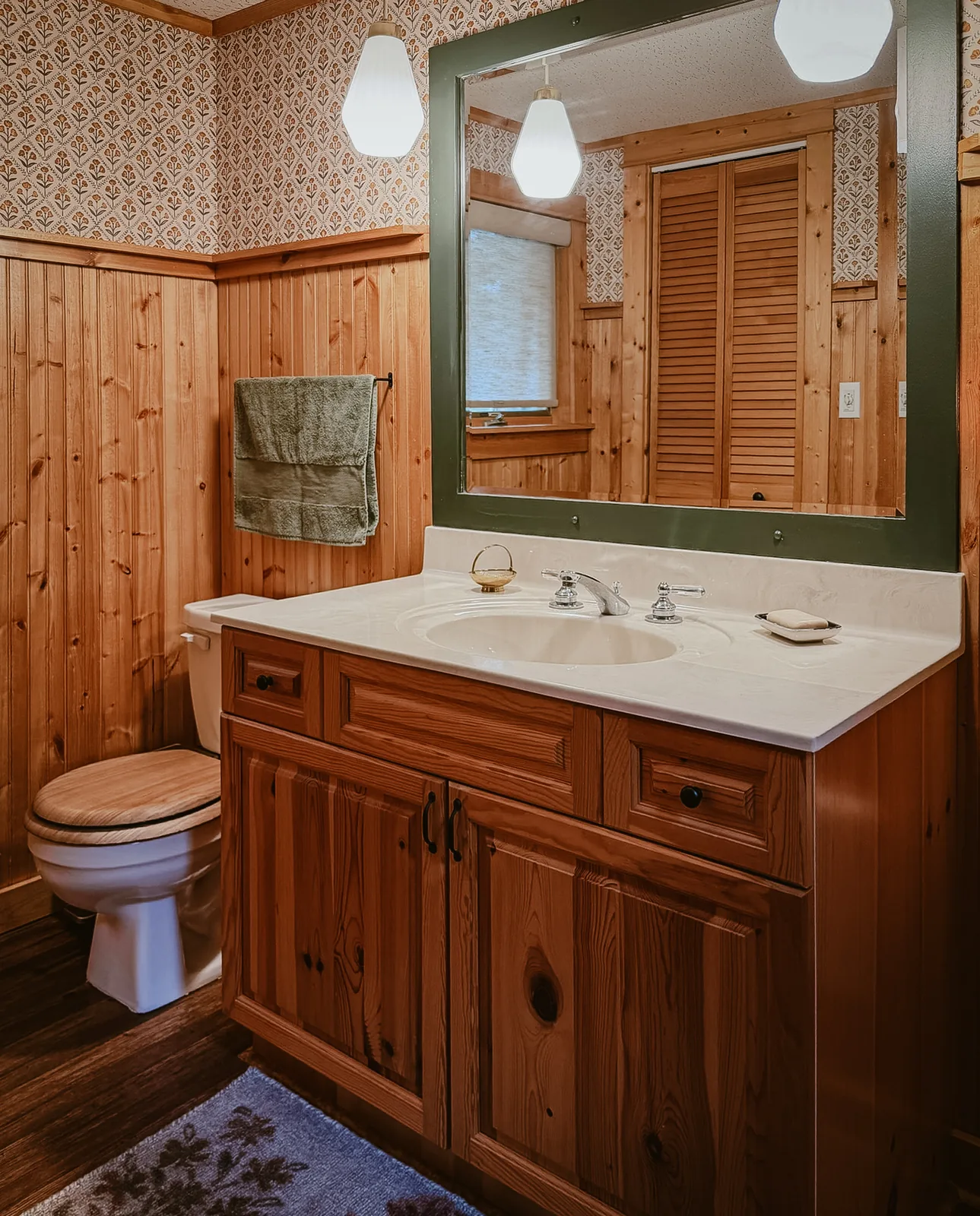 The cabin bathroom with wood-paneled walls and a green-trimmed mirror