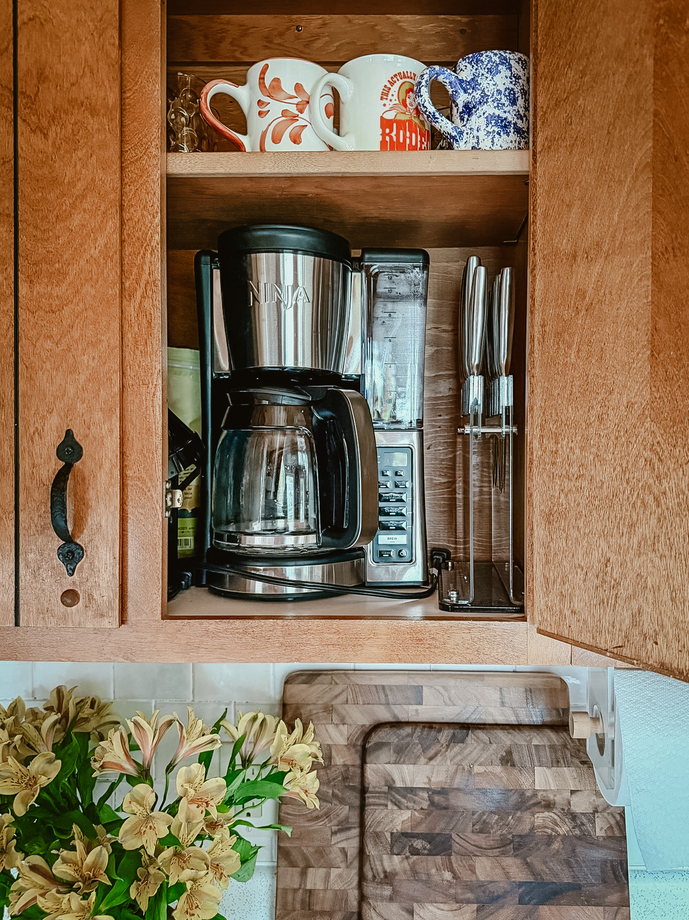 Coffee maker, bean grinder, mugs, and knives in the kitchen cabinet